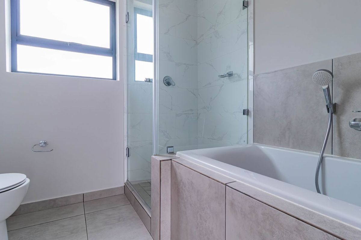 Modern bathroom featuring a glass-enclosed shower, a built-in bathtub with handheld showerhead, and neutral floor tiling.