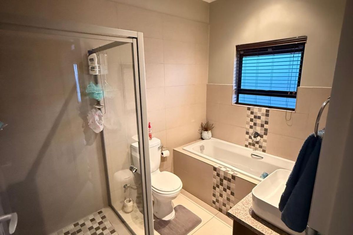 A functional bathroom featuring a glass-enclosed shower, a built-in bathtub with mosaic tile accents, a vanity basin, and a toilet.