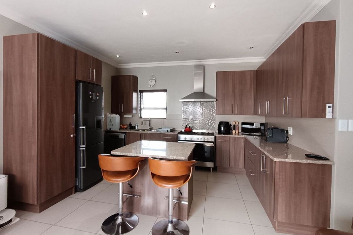 Modern kitchen featuring wood-finish cabinetry, granite countertops, a central island, stainless steel extractor fan, and tiled flooring.