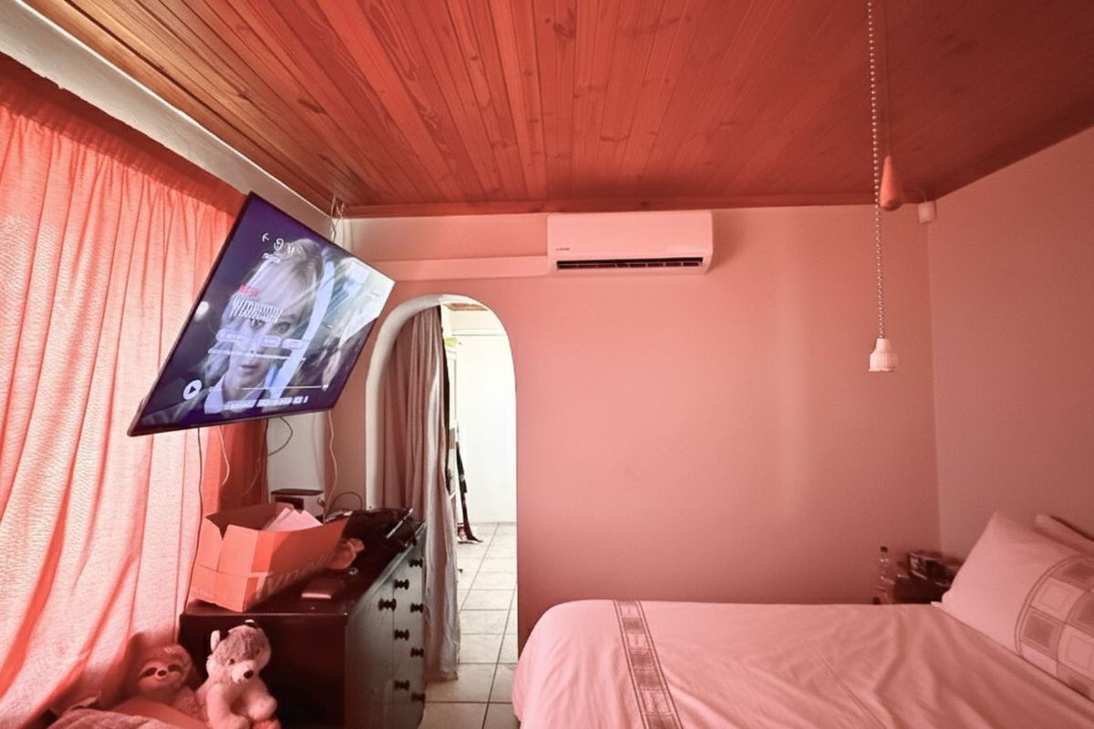 A bedroom featuring a timber-clad ceiling, wall-mounted air conditioning unit, and an arched doorway leading to an adjacent space.