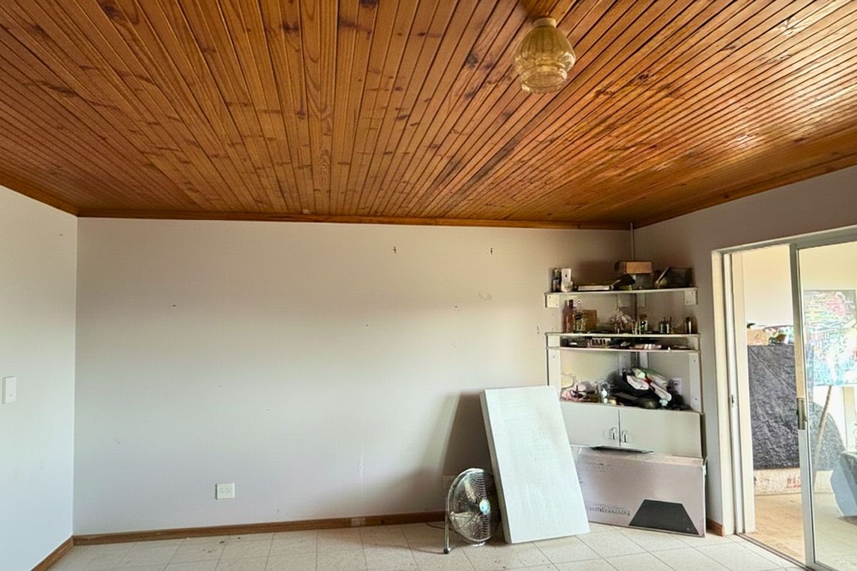 A living room featuring a timber-clad ceiling, tiled flooring, and sliding glass doors leading to an outdoor area.