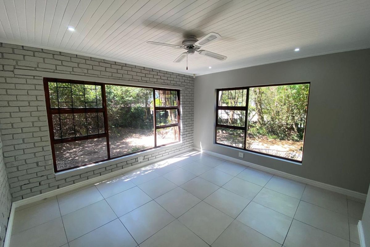 Bright living room featuring large windows, tiled flooring, a painted brick feature wall, and a ceiling fan.