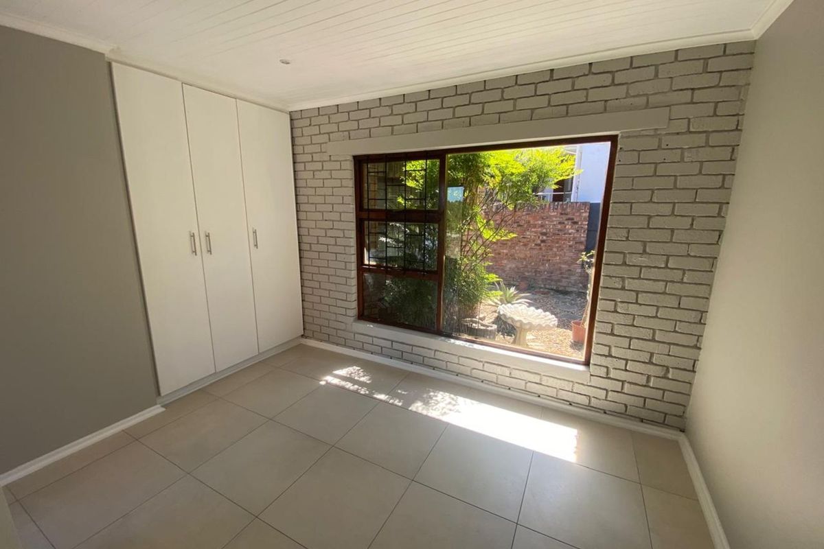 A bright bedroom featuring tiled flooring, built-in cupboards, and a large window with a view of the garden.