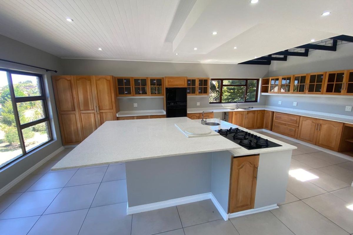 Spacious kitchen featuring extensive wooden cabinetry, a large central island with a built-in gas hob and sink, and modern tiled flooring.