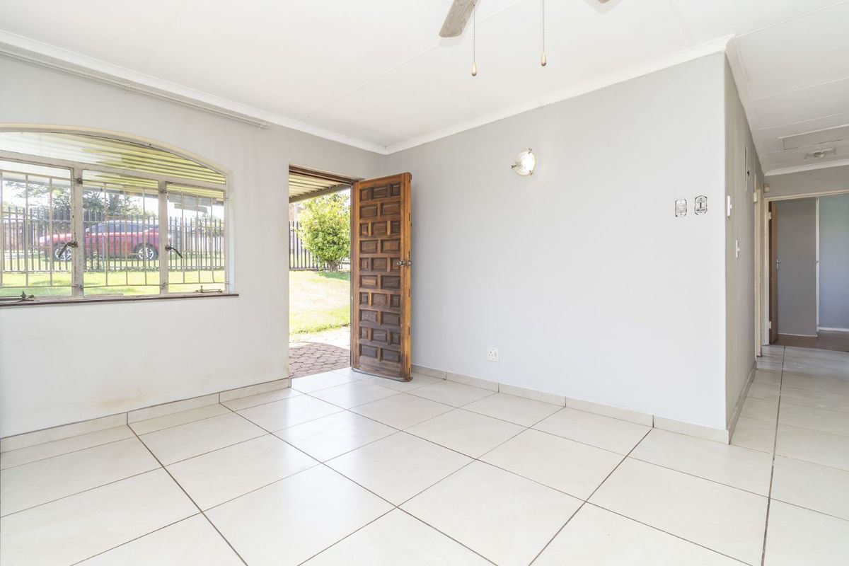 A bright, tiled living area featuring a solid wood entrance door, arched window with security bars, and a ceiling fan.