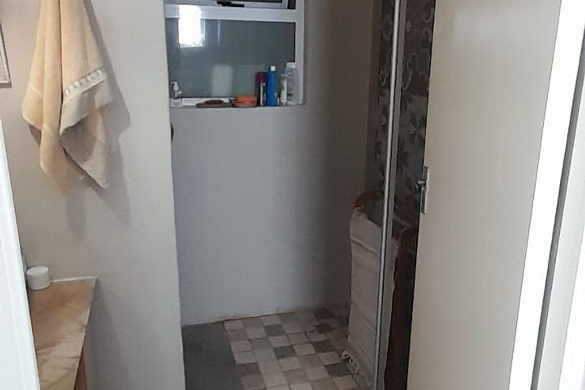 A compact bathroom featuring a shower enclosure, vanity unit, and window, currently presenting with dated finishes and basic fixtures.