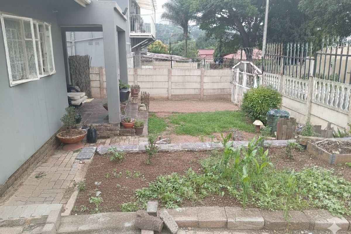 A rear garden area featuring a covered patio, paved walkways, and established garden beds enclosed by a perimeter wall.