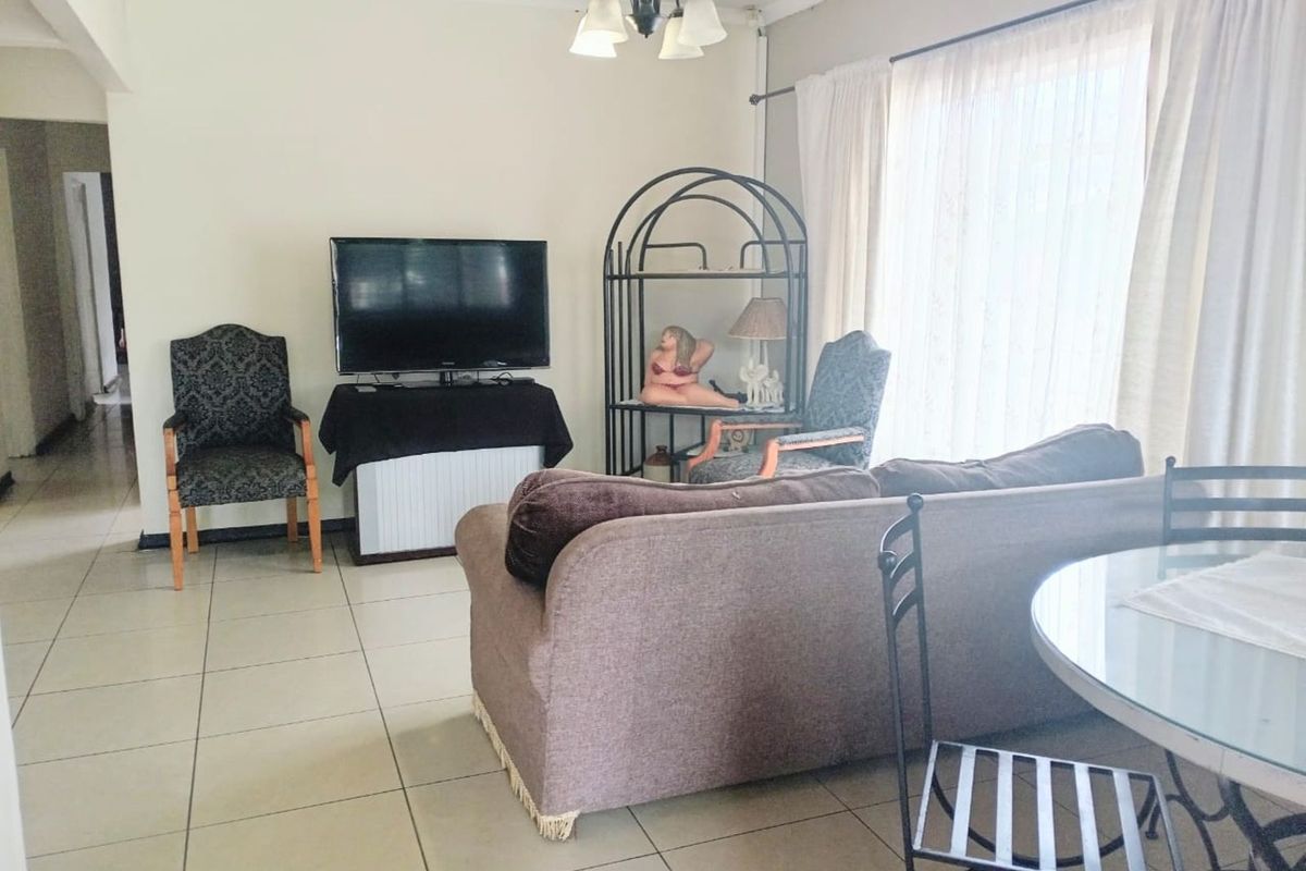 A living area featuring tiled flooring, a ceiling-mounted light fixture, and large windows with curtains, providing a functional and open living space.