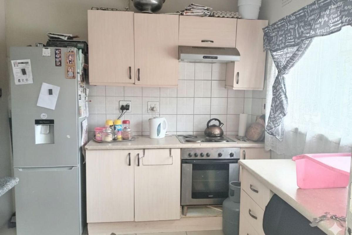 Compact kitchen featuring light-toned cabinetry, tiled backsplash, built-in oven with extractor fan, and tiled flooring.