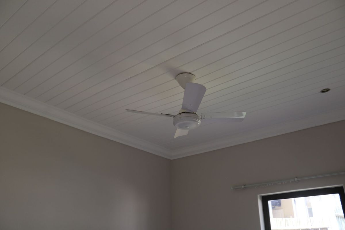 A bedroom interior featuring a white tongue-and-groove ceiling, a ceiling fan, and a window with a curtain rod.