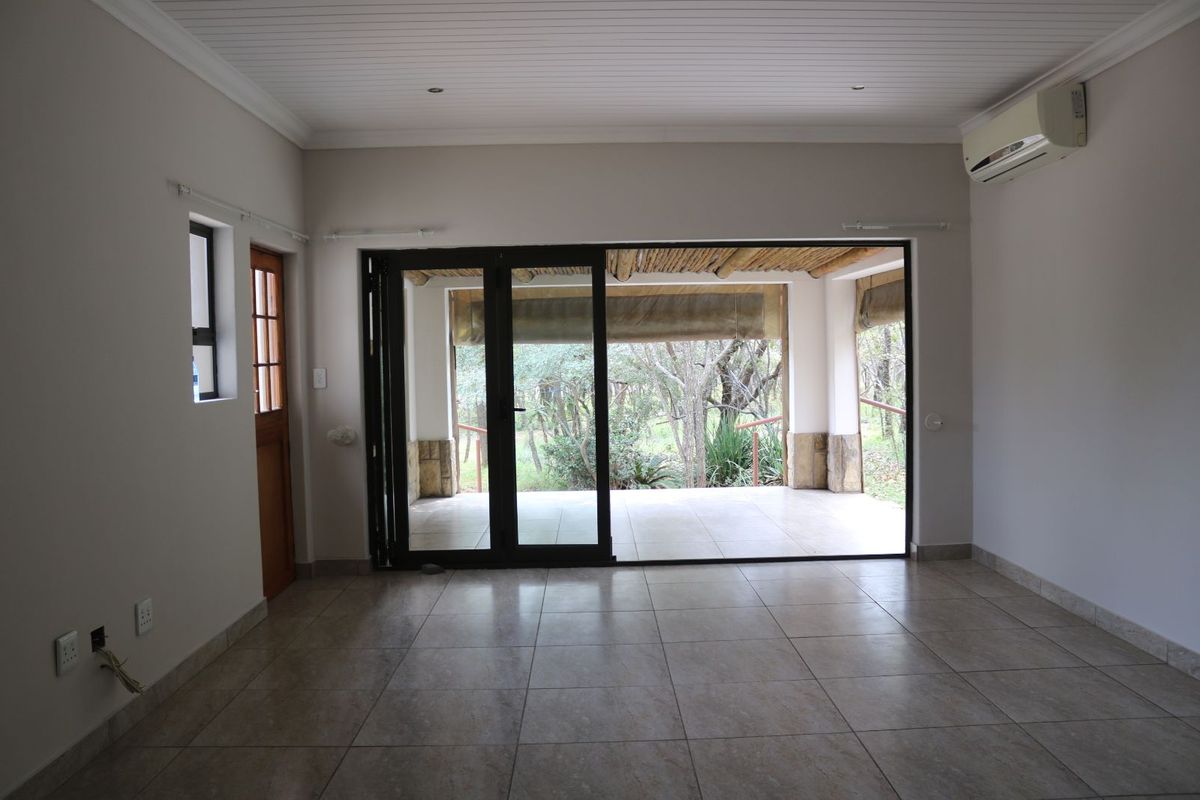 An open-plan living area featuring tiled flooring, a tongue-and-groove ceiling, wall-mounted air conditioning, and large sliding doors opening onto a covered patio.