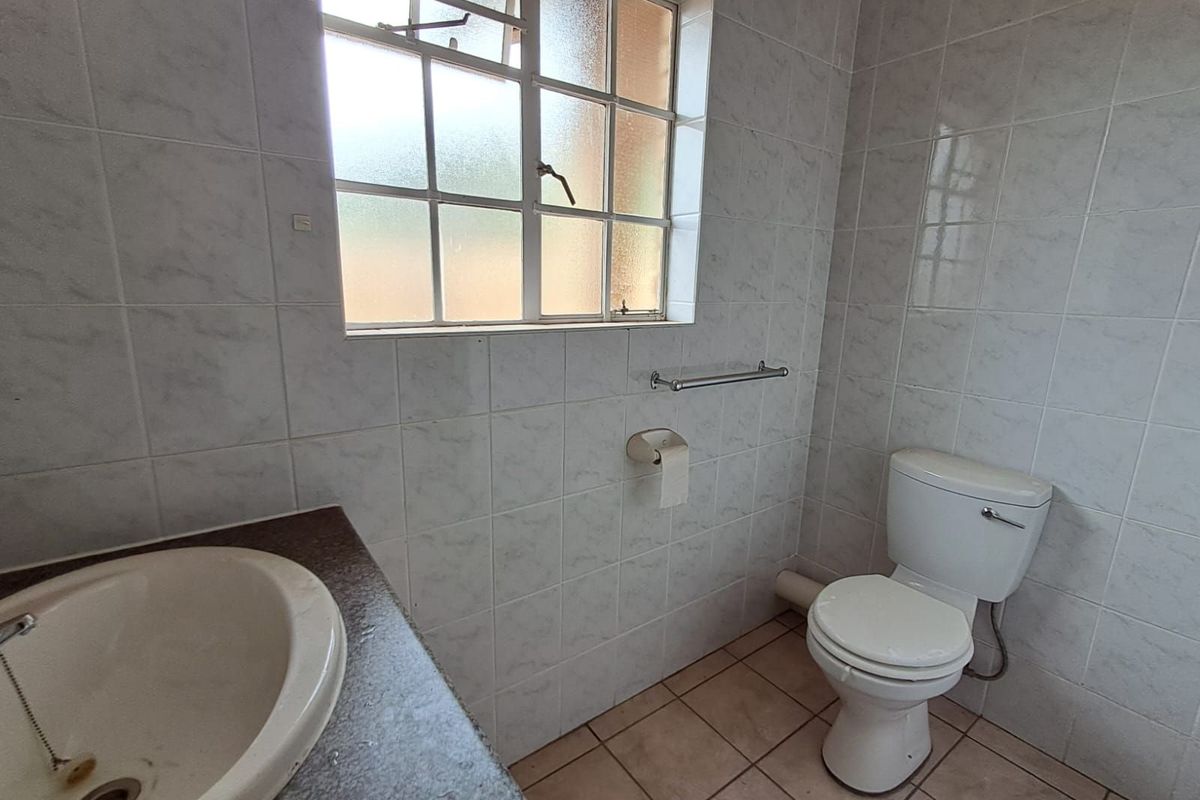 A functional bathroom featuring tiled walls, a built-in vanity with a sink, and a standard toilet under a window.