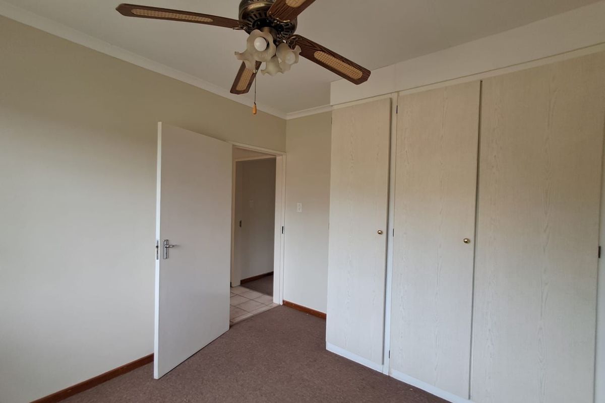 A bedroom featuring built-in cupboards, a ceiling fan, and carpeted flooring, providing a functional and neutral living space.