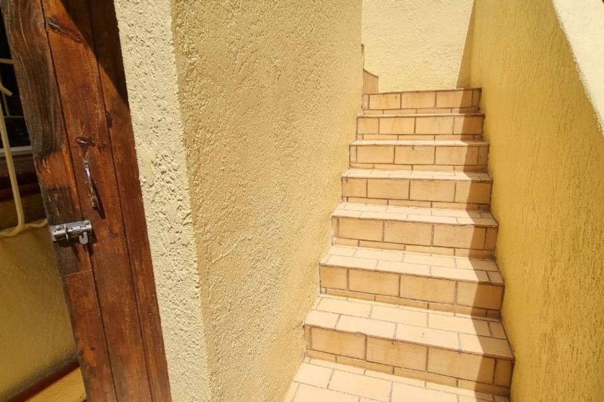 Exterior staircase with tiled steps leading to an upper level, featuring textured yellow walls and a wooden door with security bars.