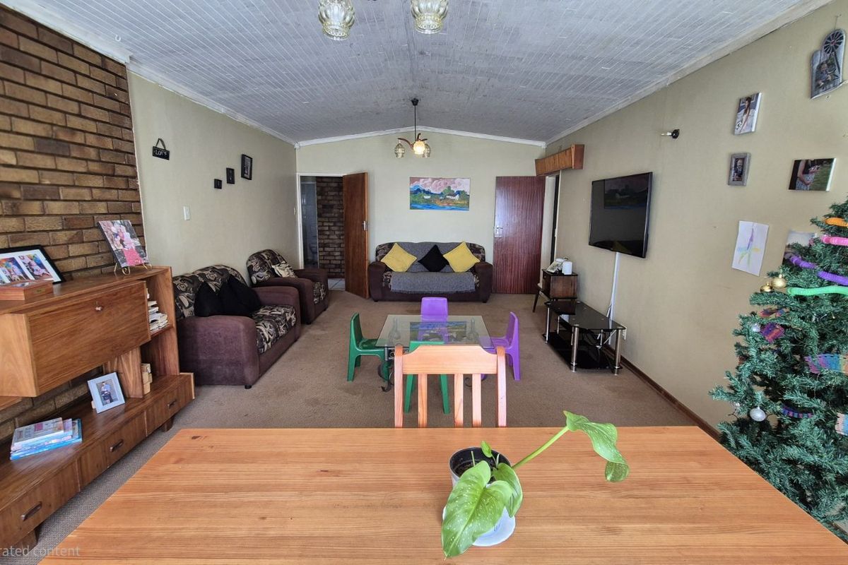 A spacious living area featuring a prominent brick feature wall, carpeted flooring, and a textured ceiling, offering a functional layout for family living.