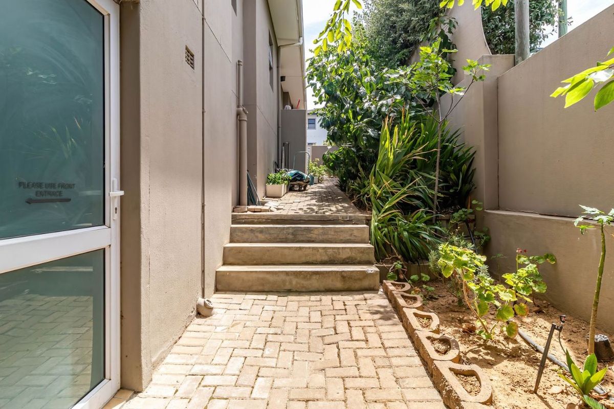 A side walkway featuring paved steps, a boundary wall, and established garden beds leading along the side of the property.