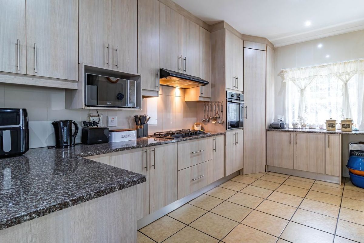 A functional kitchen featuring light wood-grain cabinetry, granite countertops, a built-in oven, gas hob, and extractor fan with tiled flooring.