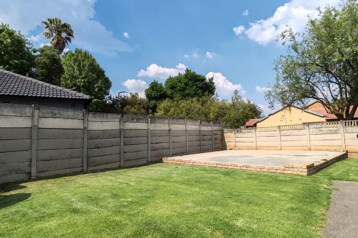 Spacious rear garden featuring a well-maintained lawn and a raised brick-edged patio area, enclosed by concrete boundary walls.