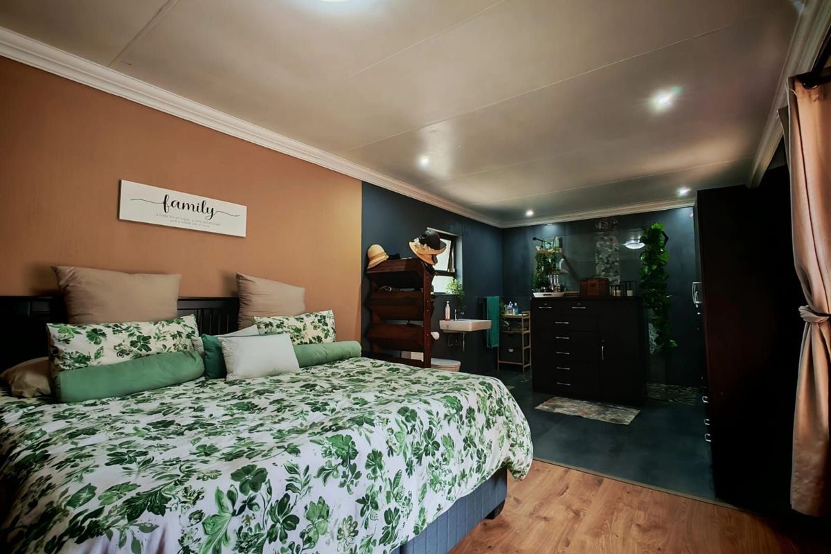A bedroom featuring laminate flooring, dual-tone painted walls, and an integrated open-plan bathroom area with a wall-mounted basin.