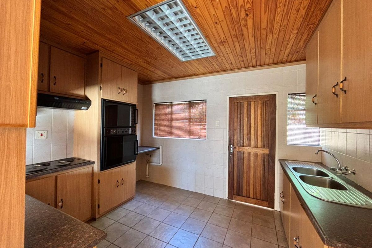 A functional kitchen featuring built-in cabinetry, a double sink, integrated oven, and hob, with tiled flooring and a timber-paneled ceiling.