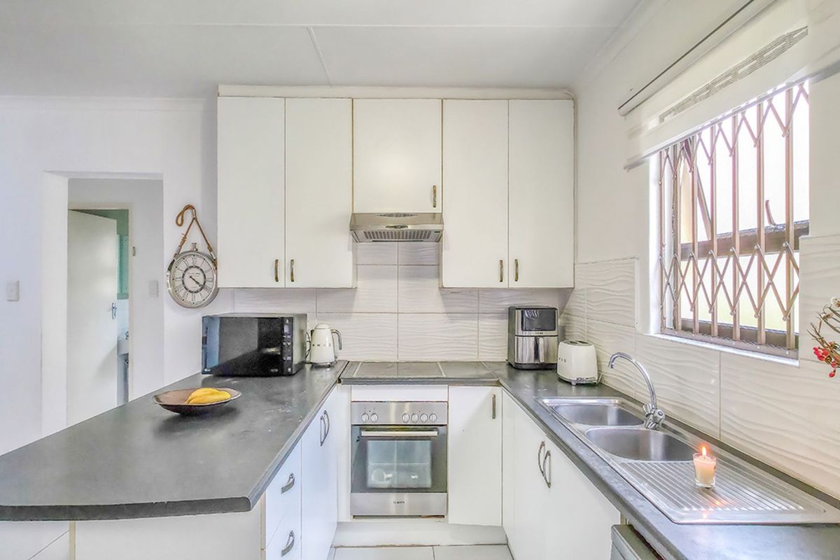 A functional kitchen featuring white cabinetry, dark countertops, a built-in oven, hob, extractor fan, and a stainless steel double sink.