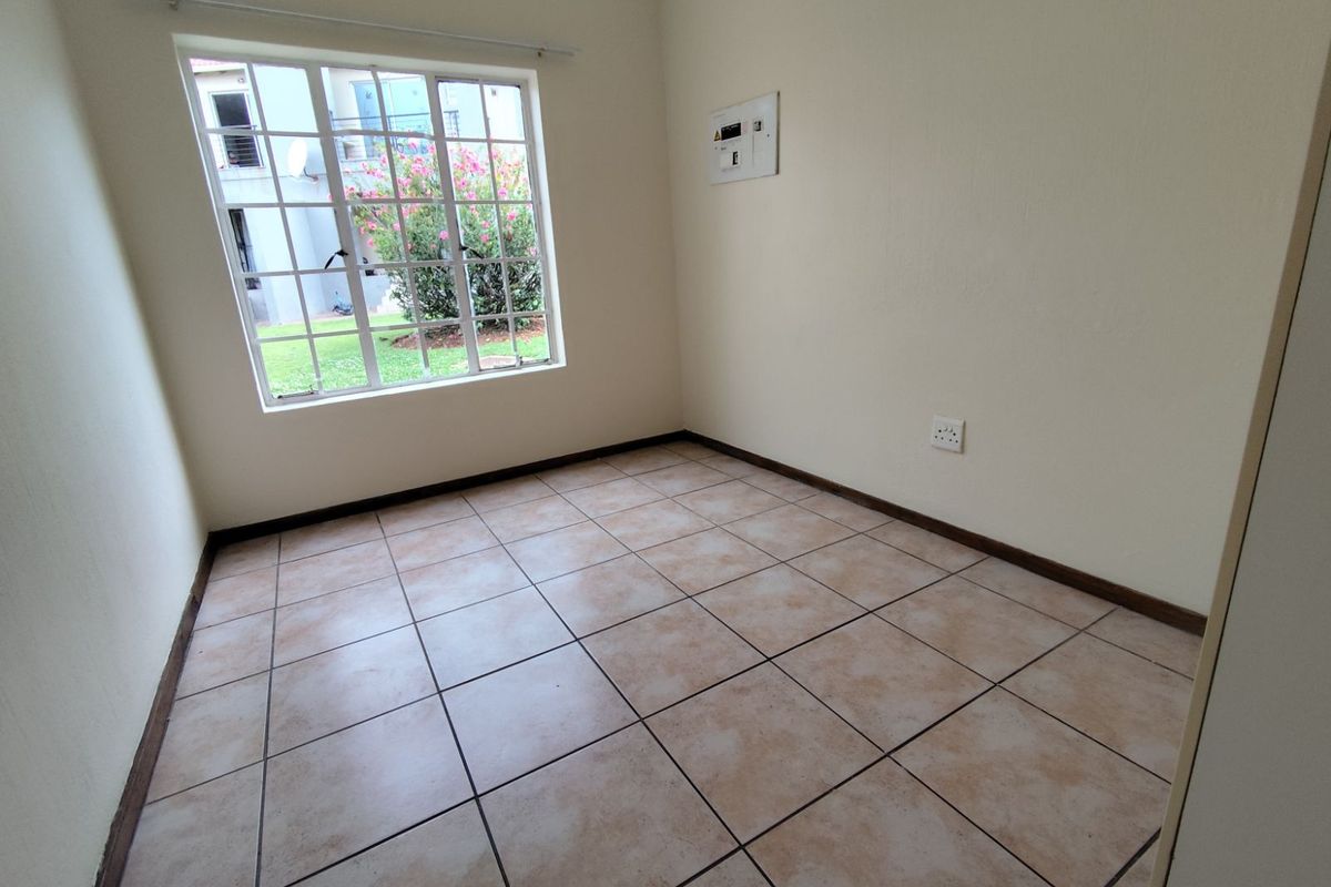 A vacant bedroom featuring neutral walls, tiled flooring, and a window overlooking the complex grounds.