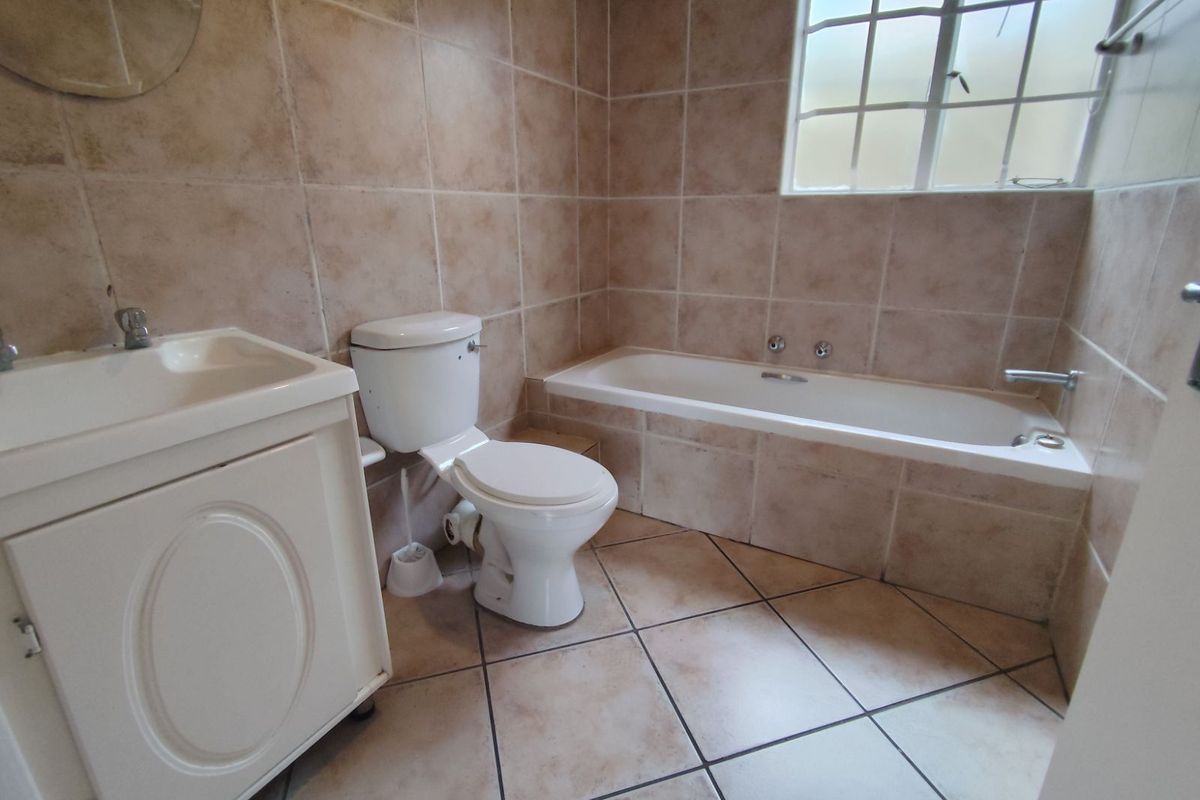 A functional bathroom featuring a built-in bathtub, a vanity basin, and a toilet, finished with neutral wall and floor tiling.