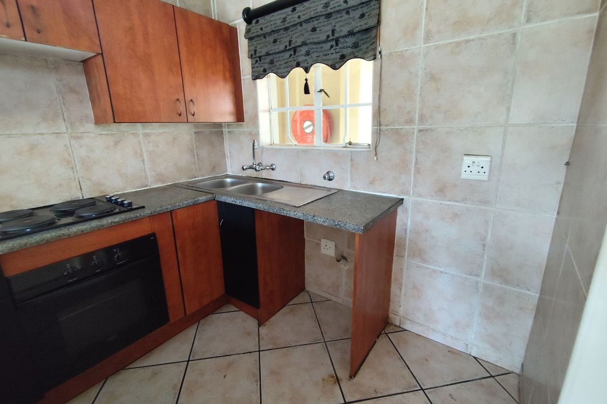 A functional kitchen featuring wood-finish cabinetry, granite-look countertops, a built-in oven and hob, and tiled splashbacks with a double sink.