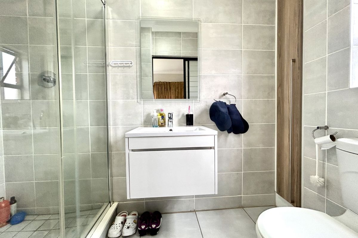 Modern bathroom featuring a wall-mounted vanity, glass-enclosed shower, neutral wall tiling, and a built-in storage cabinet.