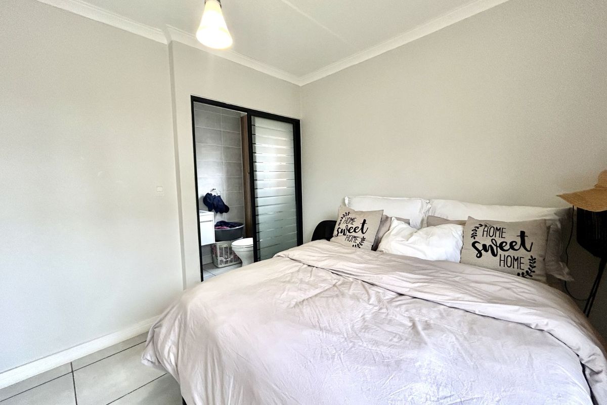A well-maintained bedroom featuring tiled flooring, neutral walls, and an en-suite bathroom accessed through a sliding door.