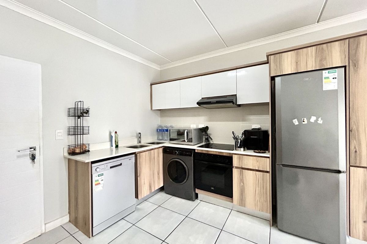 Modern kitchen featuring light wood-grain cabinetry, white countertops, integrated oven, hob, extractor fan, and dedicated space for a dishwasher and washing machine.