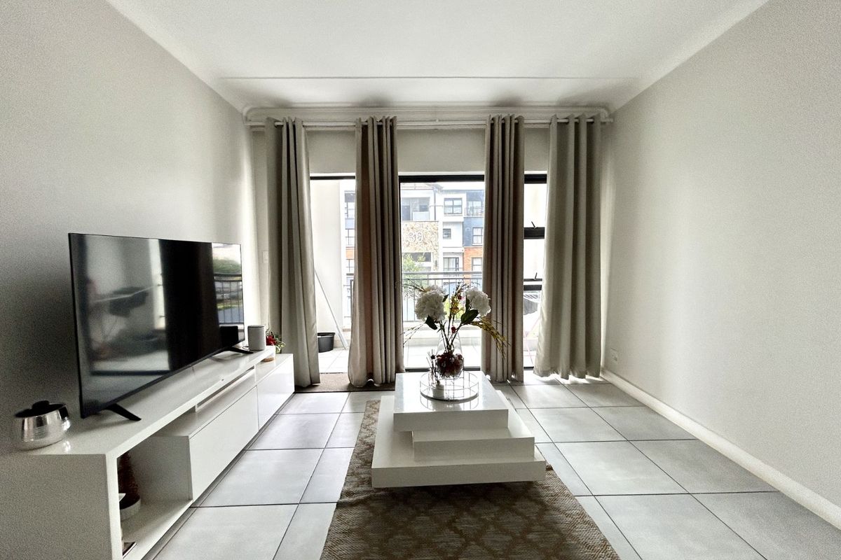 A bright living room featuring large glass sliding doors leading to a balcony, neutral tiled flooring, and clean white walls.