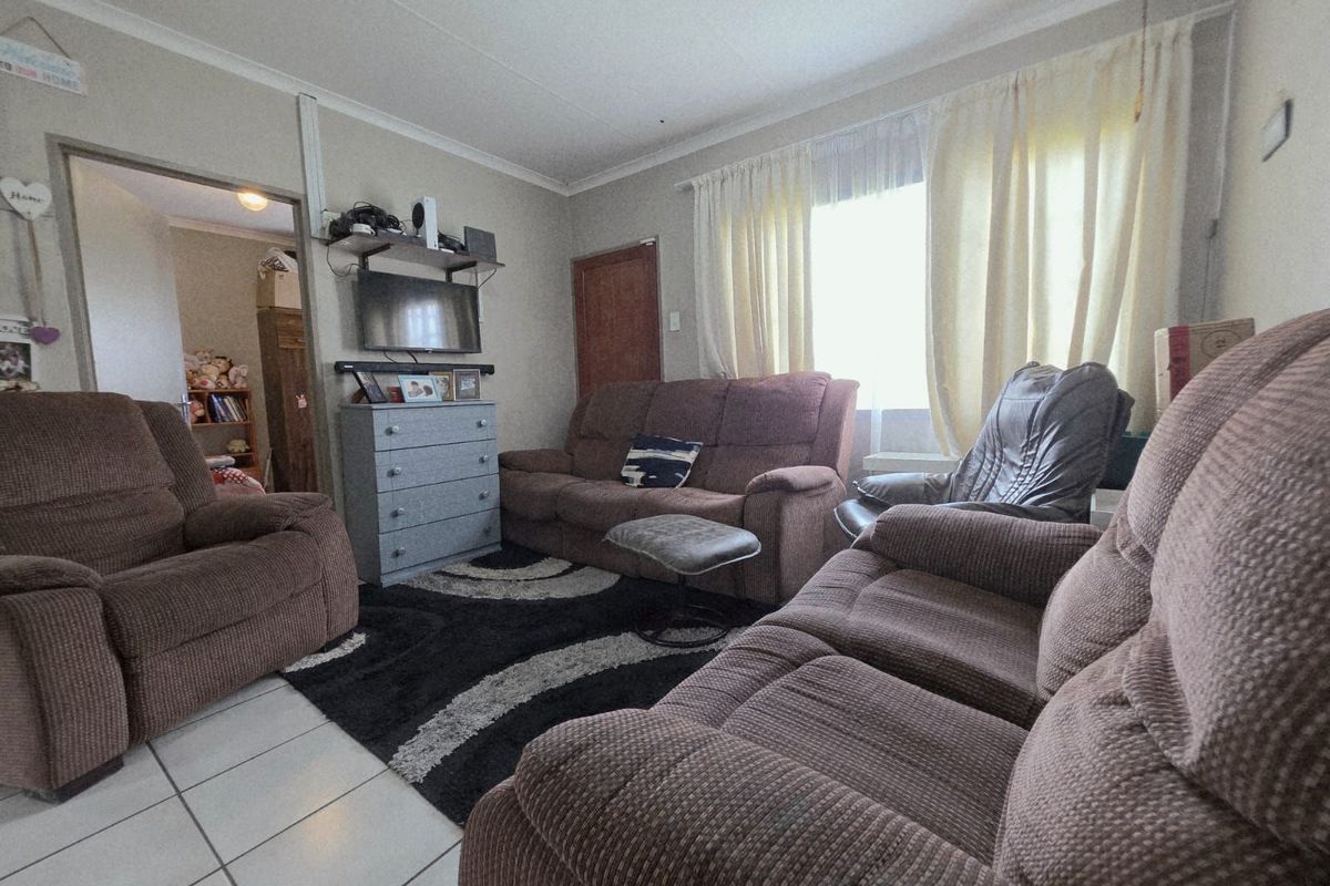 A comfortable living room featuring tiled flooring, neutral wall finishes, and a large window allowing for natural light.
