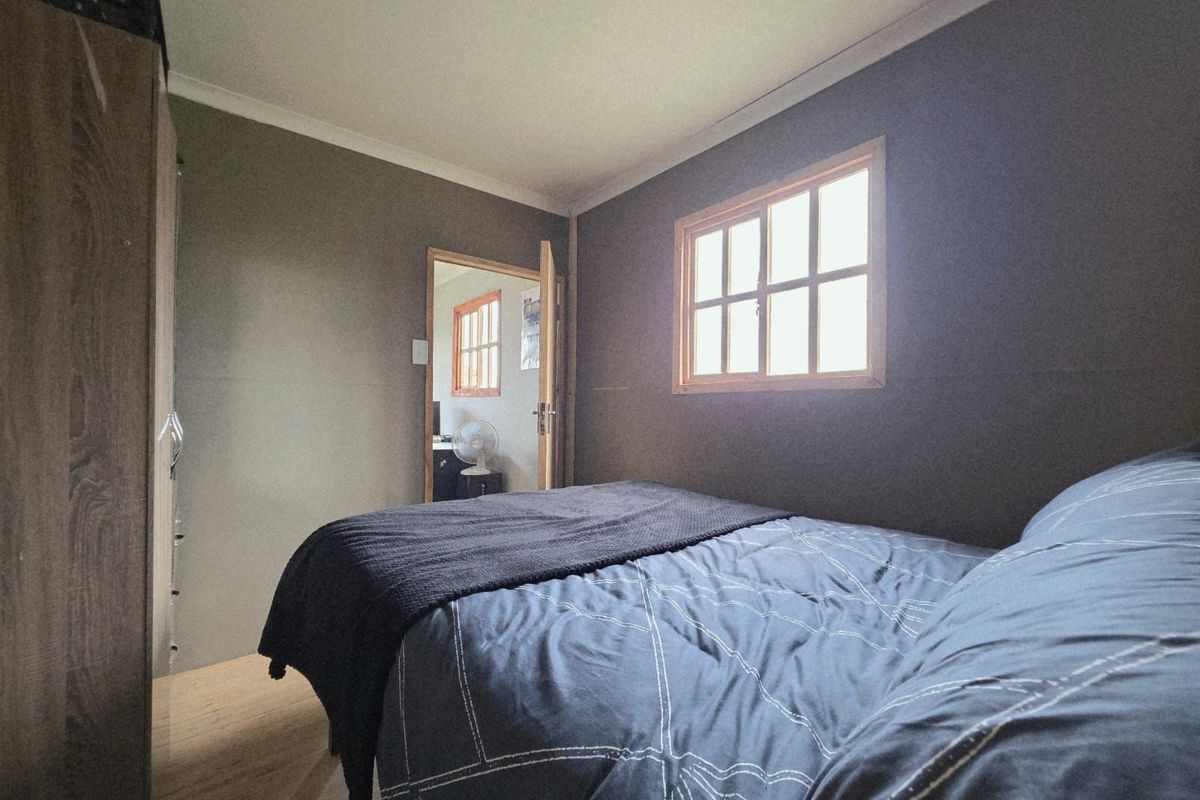 A bedroom featuring dark-toned walls, a wooden-framed window, and a built-in wardrobe, providing a cozy and functional sleeping space.
