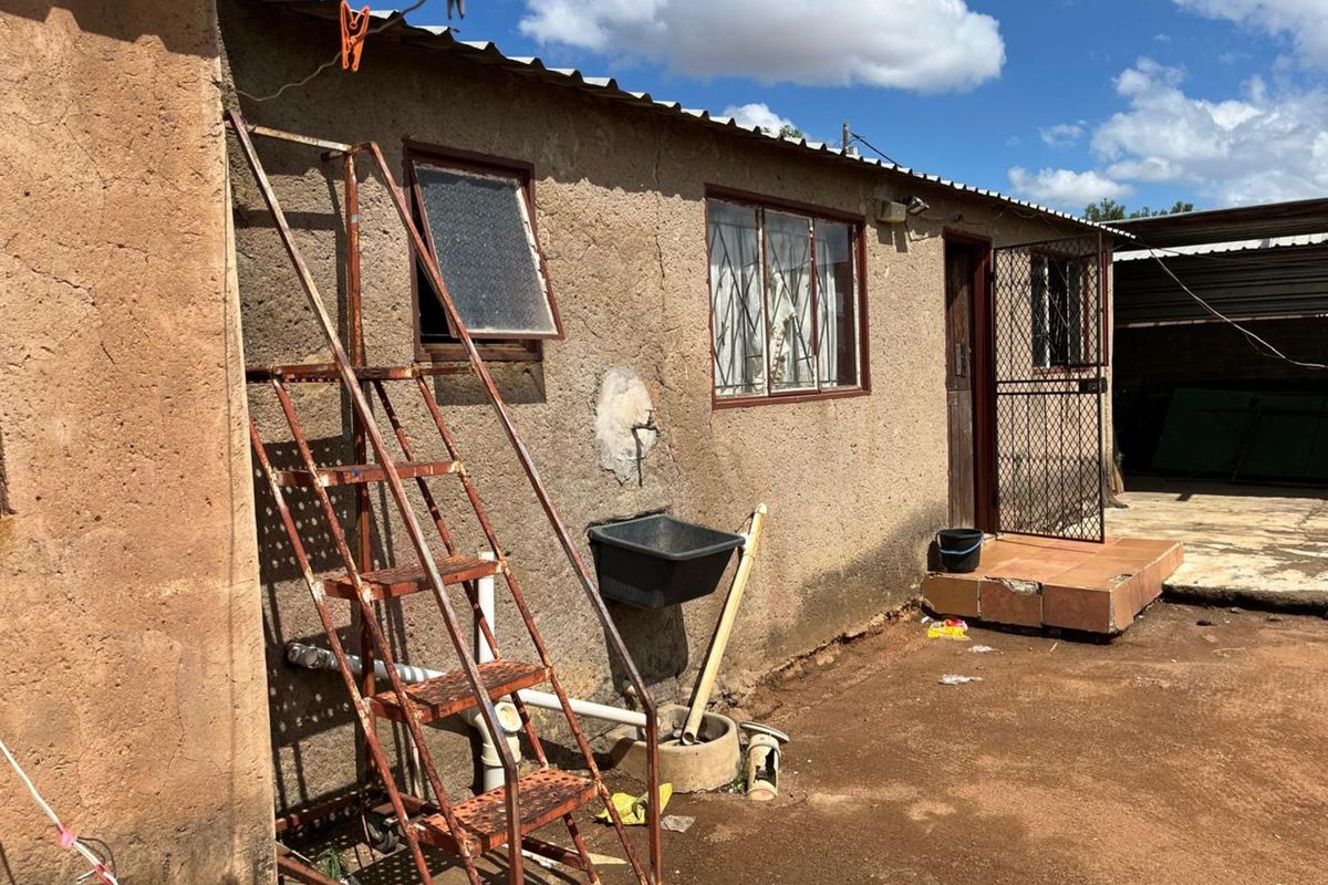 Rear exterior view of the property featuring a textured wall finish, security gate, and basic utility plumbing fixtures.