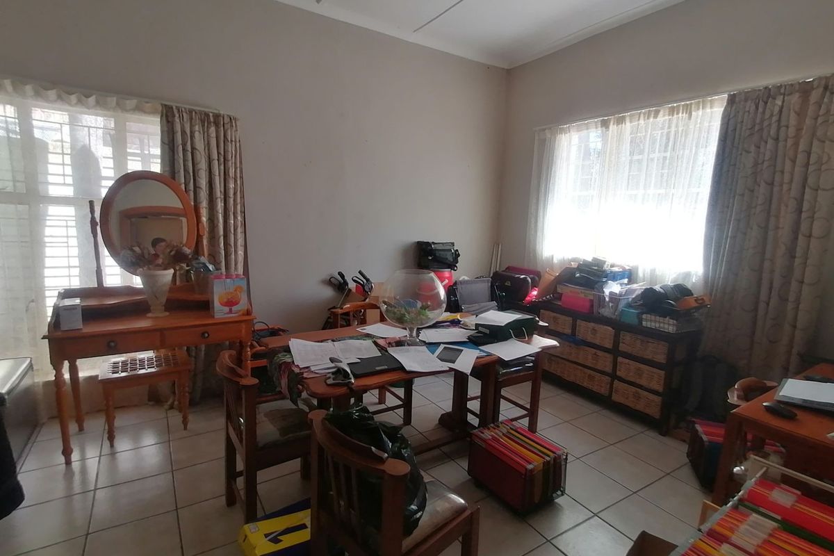 A multi-purpose room featuring tiled flooring and large windows with security bars, suitable for use as a bedroom, office, or study area.