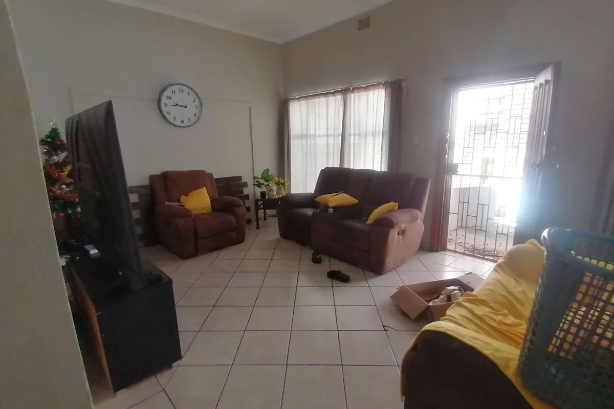 A living room featuring tiled flooring, large windows with curtains, and a security gate leading to the exterior.