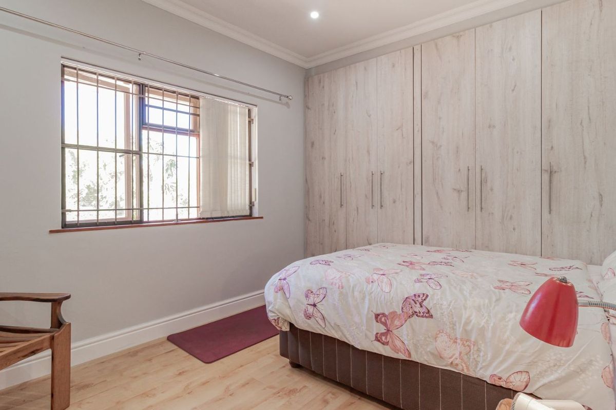 A well-maintained bedroom featuring light wood-look flooring, built-in wardrobes with a modern finish, and a window fitted with security bars.