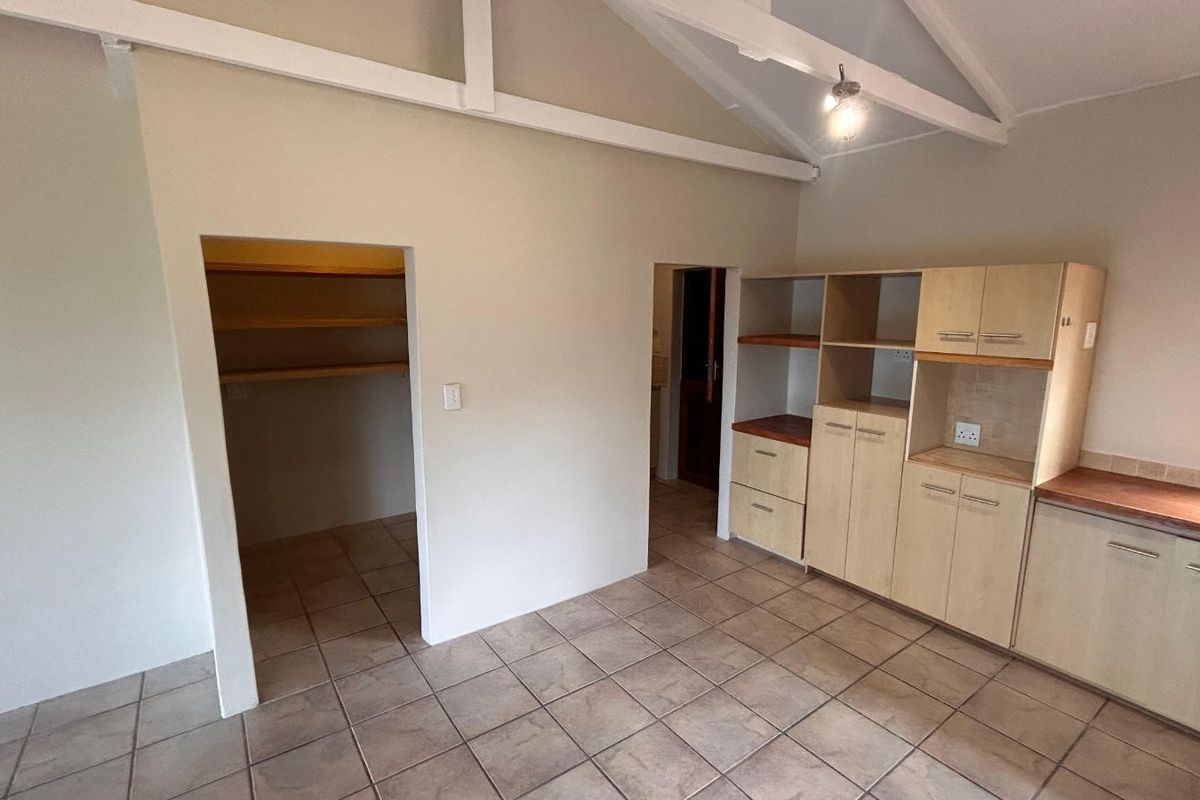 A functional kitchen area featuring built-in cabinetry, tiled flooring, and a walk-in pantry with exposed timber shelving under a vaulted ceiling.
