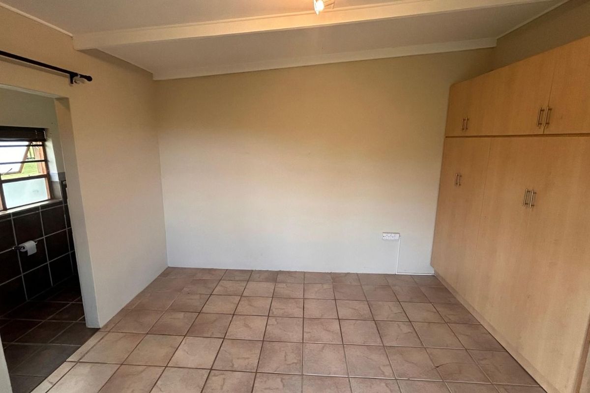 A bedroom featuring built-in wooden cupboards, tiled flooring, and an adjoining bathroom area.