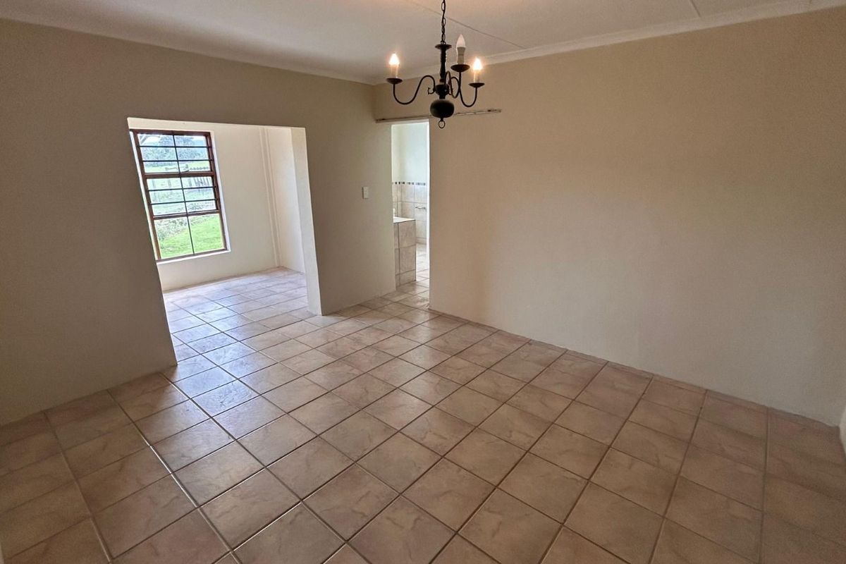 A spacious, tiled living area featuring neutral walls, a classic chandelier, and an open-plan layout leading to adjacent rooms.