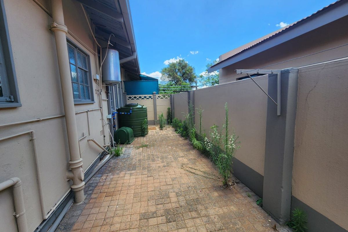 A side exterior walkway featuring paved flooring, a water storage tank, and a wall-mounted washing line, enclosed by boundary walls.