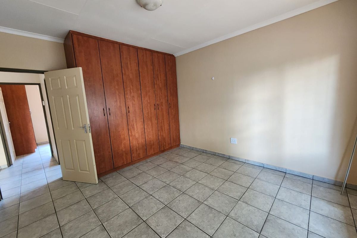 A spacious bedroom featuring built-in wooden cabinetry, neutral wall finishes, and tiled flooring, offering a clean and functional living space.