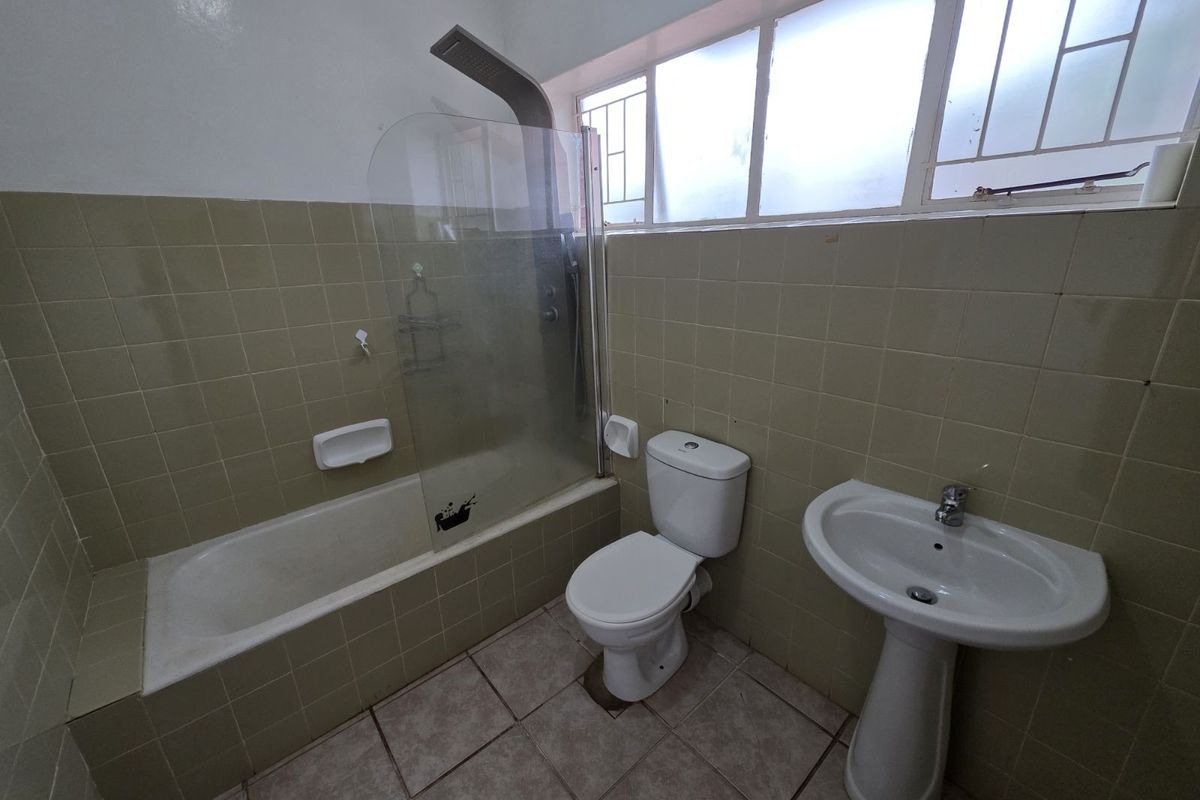A functional bathroom featuring a pedestal sink, a toilet, and a bathtub with a glass shower screen and overhead shower fixture.