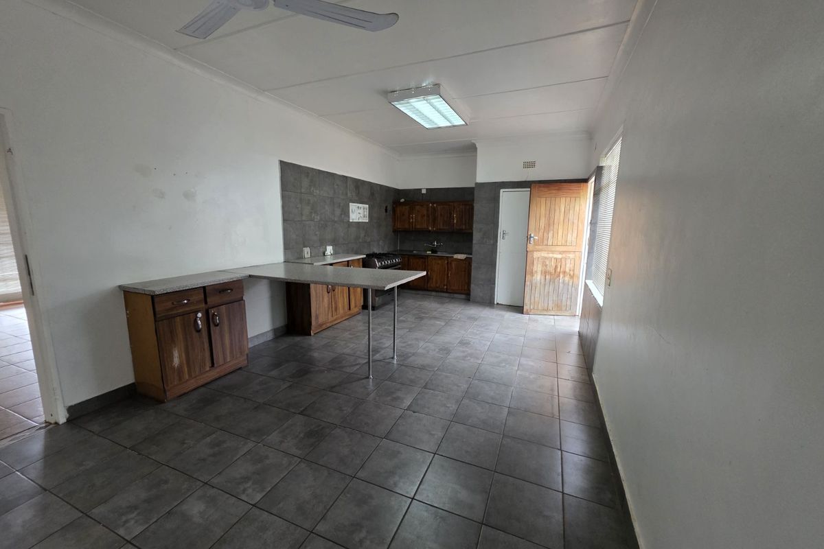 A functional kitchen featuring dark tiled flooring, wooden cabinetry, a breakfast counter, and a built-in stove, offering a practical layout for daily use.