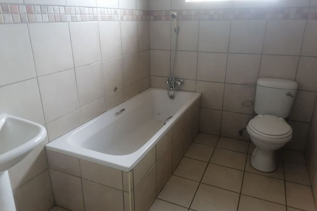 A functional bathroom featuring a built-in bathtub with handheld shower attachment, a standard toilet, and tiled walls and flooring.