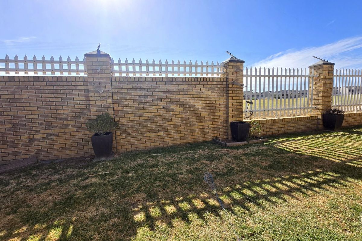 A private rear garden area featuring a sturdy face-brick boundary wall topped with white metal fencing and integrated electric security wiring.