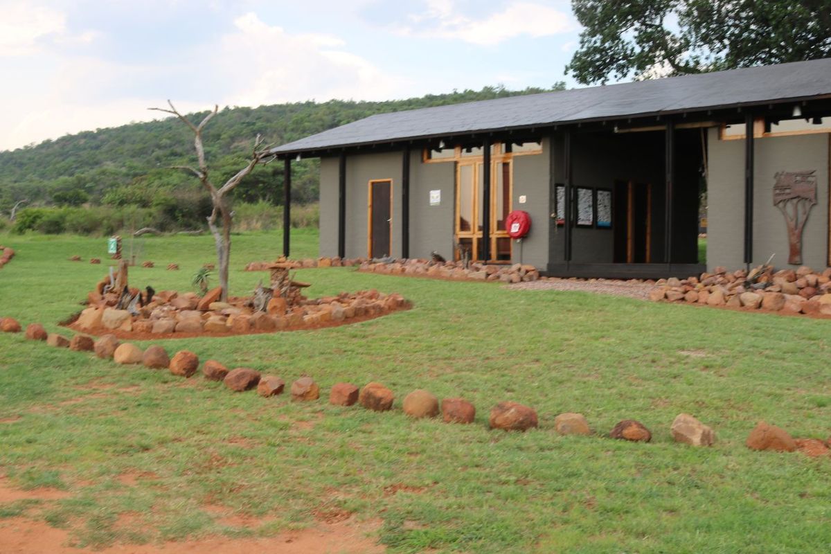 A view of the farm building exterior featuring stone masonry accents, a covered patio area, and landscaped garden surroundings.