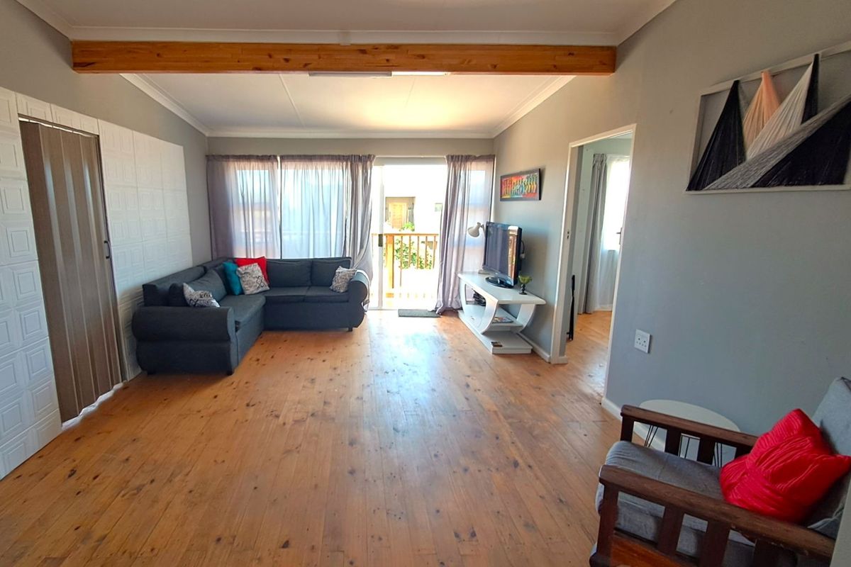 Spacious living room featuring exposed timber ceiling beams, polished wooden flooring, and sliding glass doors leading to an outdoor balcony area.