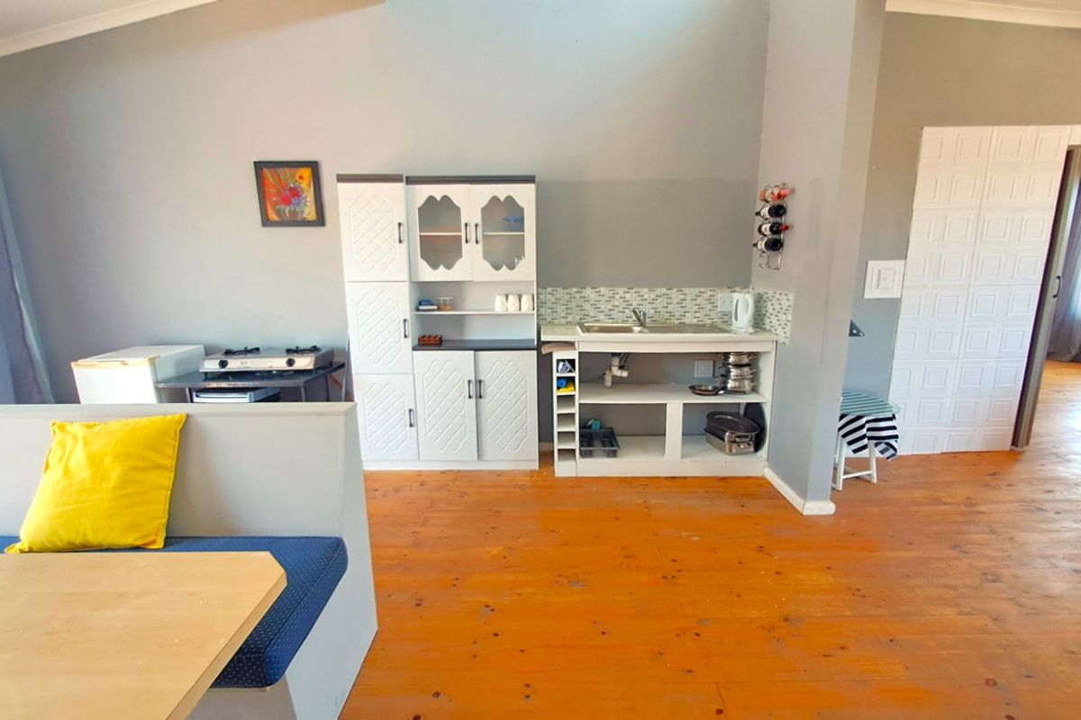 A compact kitchen area featuring a basic sink unit, open shelving, and timber flooring, integrated into a larger living space.